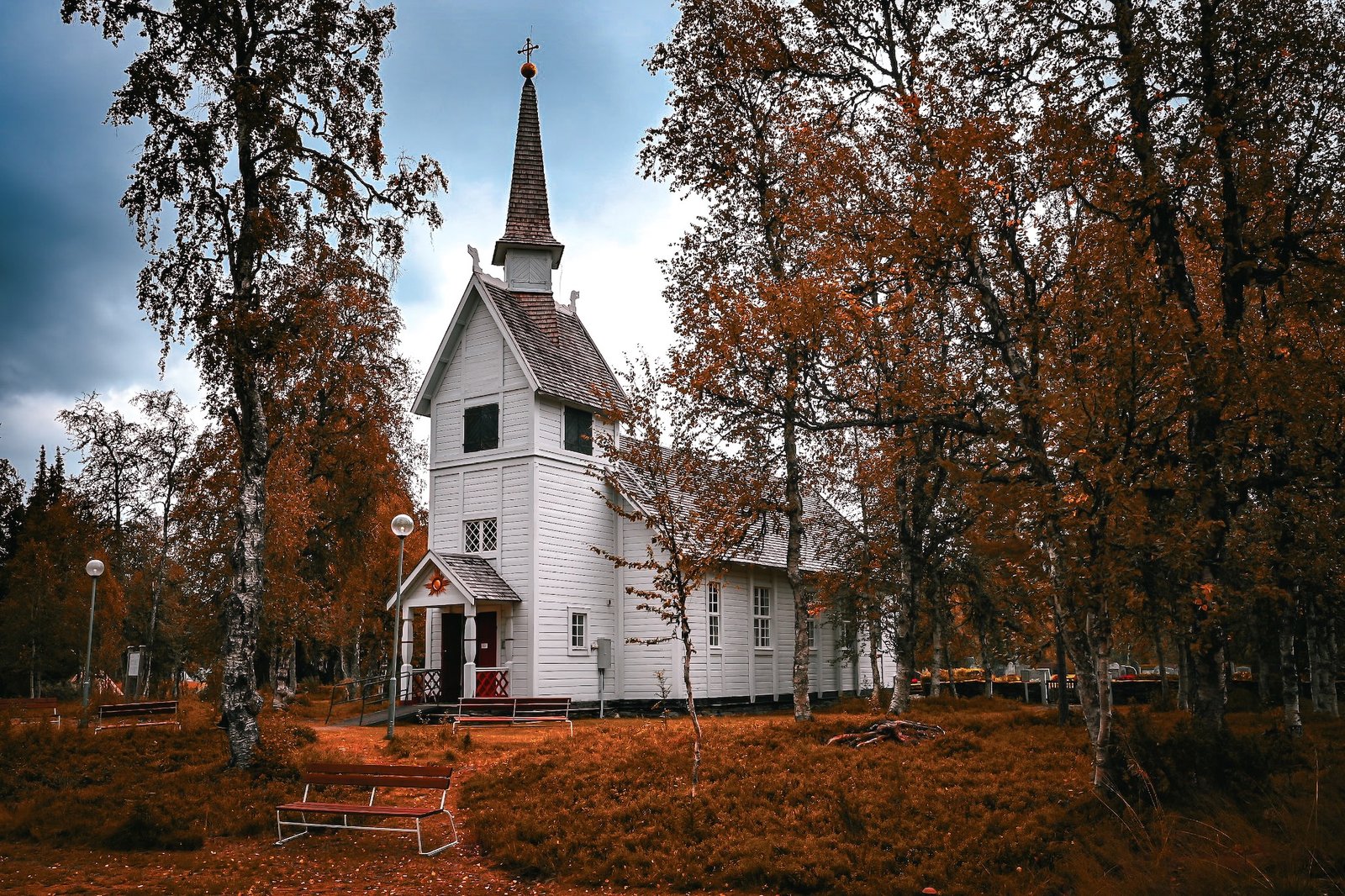 Weiße Holzkirche im Herbstwald mit warmen Kupfertönen und dramatischem Himmel.
