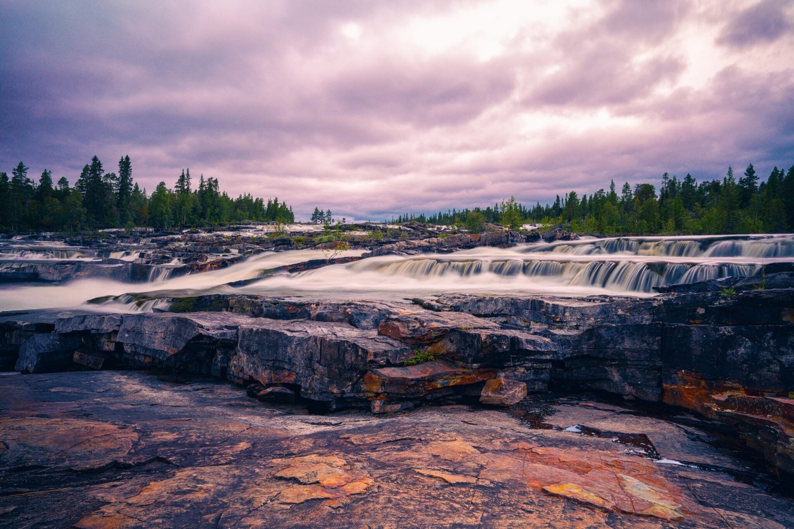 Dramatische Stromschnellen von Trappstegsforsen in Schweden mit moosbewachsenen Felsen im Vordergrund